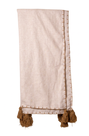 A light beige linen throw blanket with brown tassels and decorative stitching along the edges