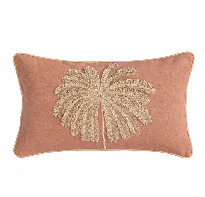 A rectangular dusty rose throw pillow featuring a large, textured beige palm leaf applique in the center, set against a plain white background.